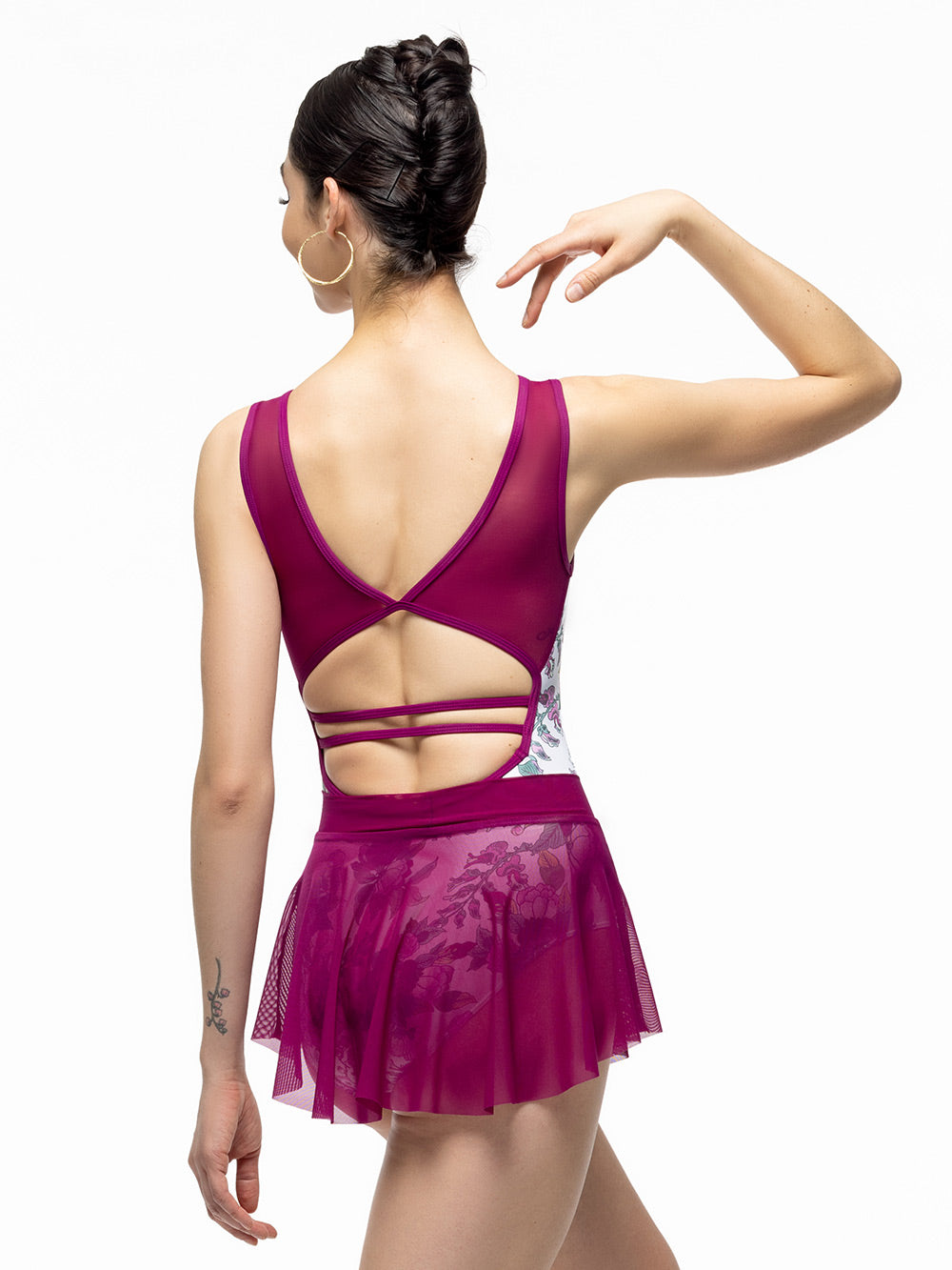 Back of model wearing magenta mini mesh skirt with wide waistband. Paired with white and magenta floral print leotard with tank straps and open strappy back.