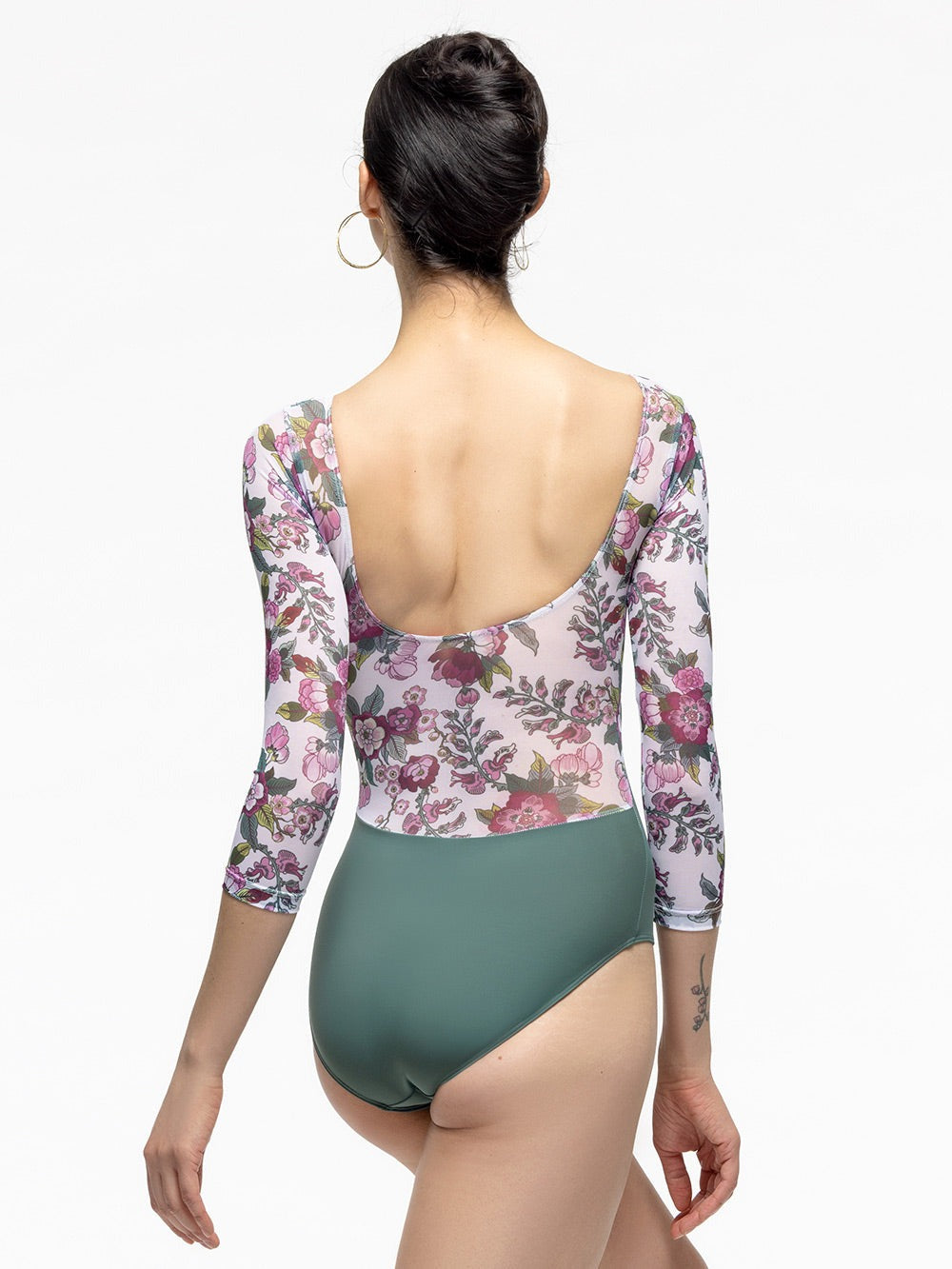 Back of model wearing pale green leotard with white, magenta, and green floral print mesh top, scoop back, and below elbow sleeves.
