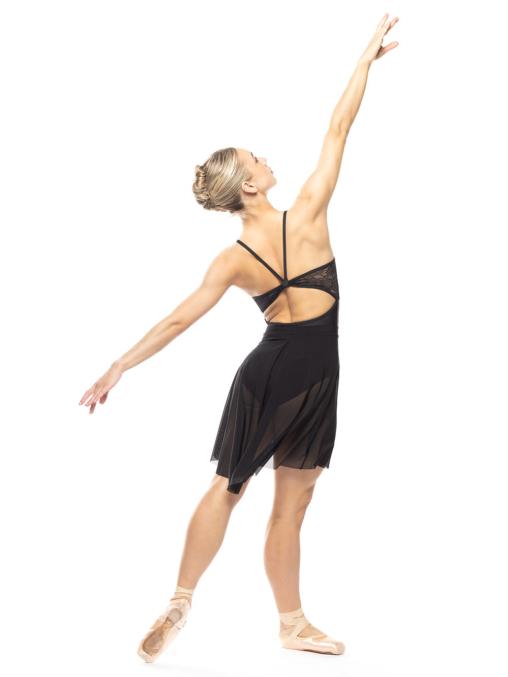 Dancer is in four arabesque profile on tendu derriere with arms extended looking diagonal up, showing back detail of the Back Tuck Skirt Black Mesh RTW.