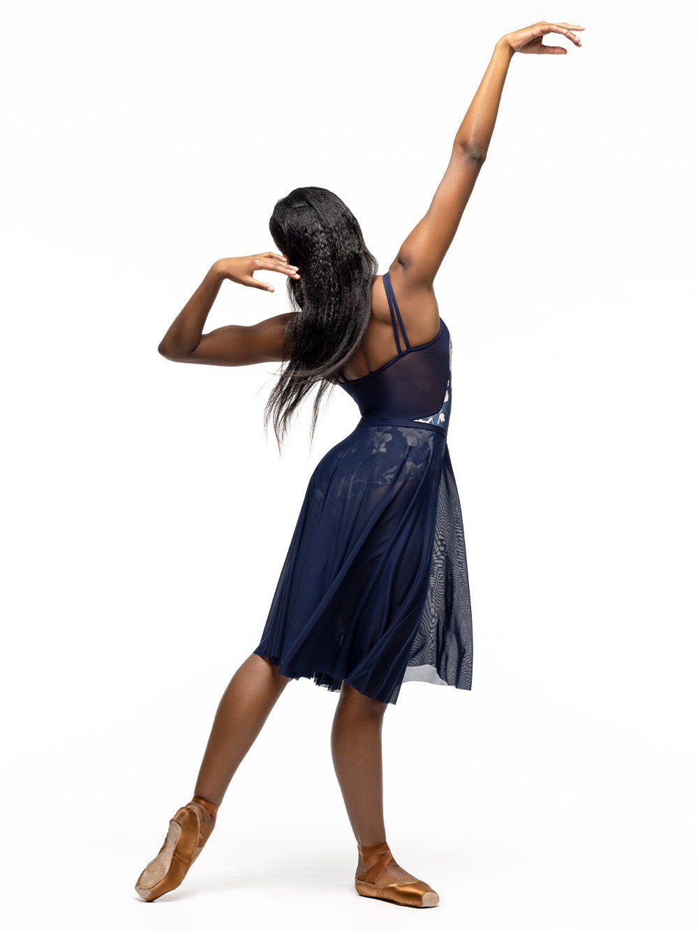 Back of model wearing dark navy blue and gold floral print bodysuit with double cami straps and blue mesh back. Paired with matching navy blue long circle mesh skirt.