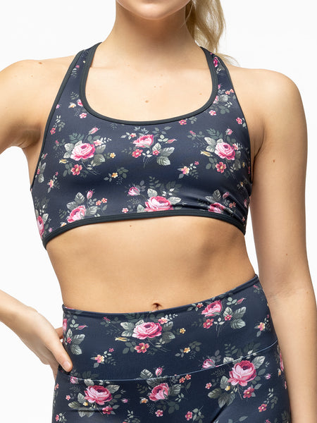 Model is wearing navy blue and pink floral print racerback sports bra with matching floral print biker shorts.