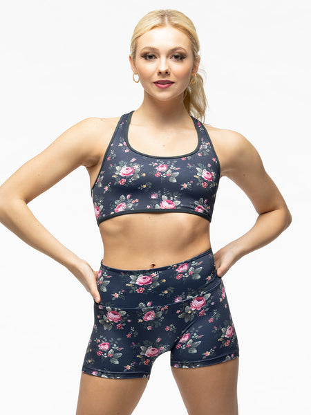 Model is wearing navy blue and pink floral print racerback sports bra with matching floral print biker shorts.