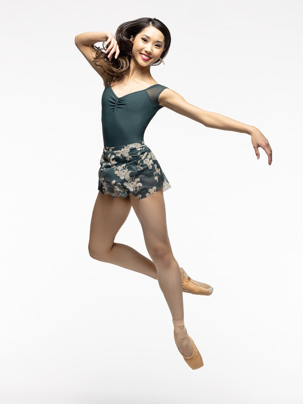 Model is wearing forest green and gold floral print mesh mini skirt paired with forest green leotard with front pinch and cap sleeves.
