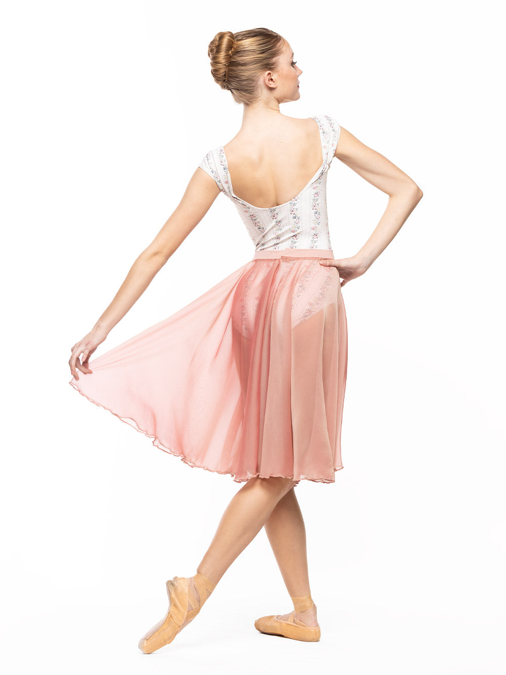 Dancer is facing back with one hand on the hip and the other one holding the Chiffon Rehearsal Skirt Sandstone RTW extended with one leg on cou-de-pie flat derriere.