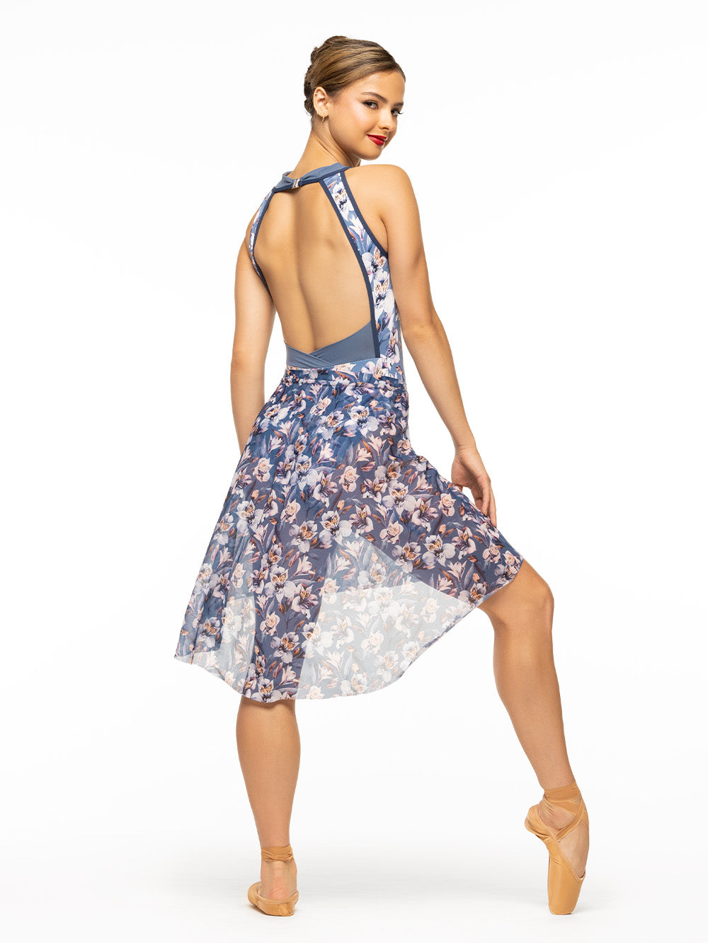 Back of model wearing blue floral print bodysuit with blue mesh high neck, navy blue trim, and open clasp back paired with matching floral mesh high low skirt.