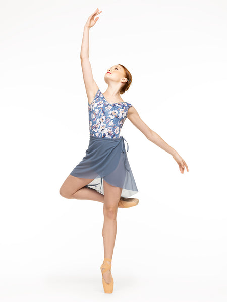 Model is wearing blue floral print bodysuit with a deep v pinch front and low back paired with denim blue mesh wrap skirt.