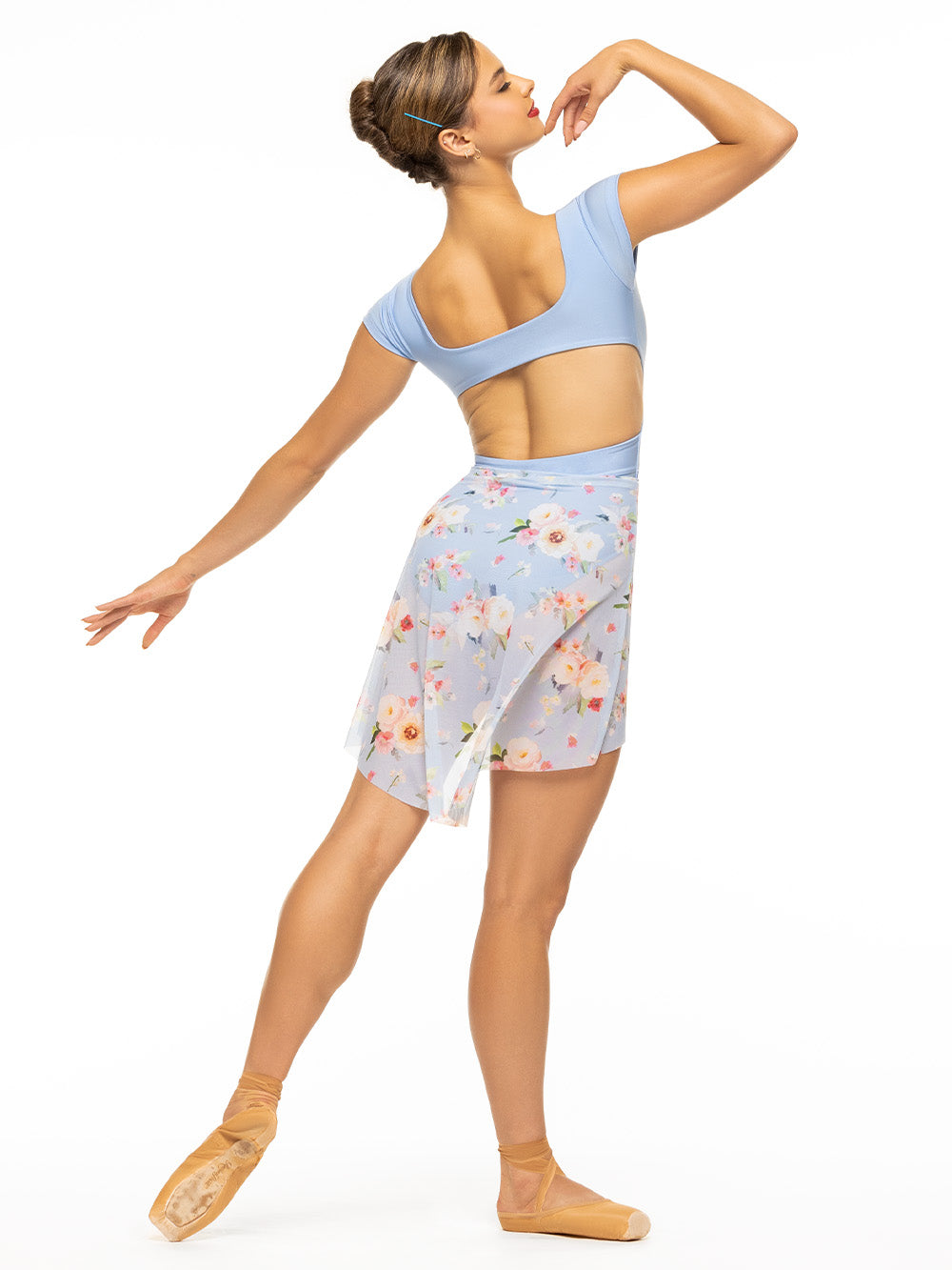 Back of model wearing shiny baby blue bodysuit with a deep v, front twist, open back, and cap sleeves paired with blue floral print mesh high low skirt.