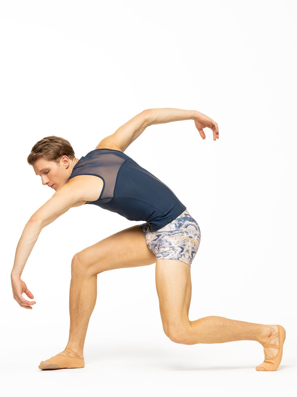 Model is wearing navy blue men's sleeveless top with mesh detail and blue, gold, and white ink swirl print activewear shorts.