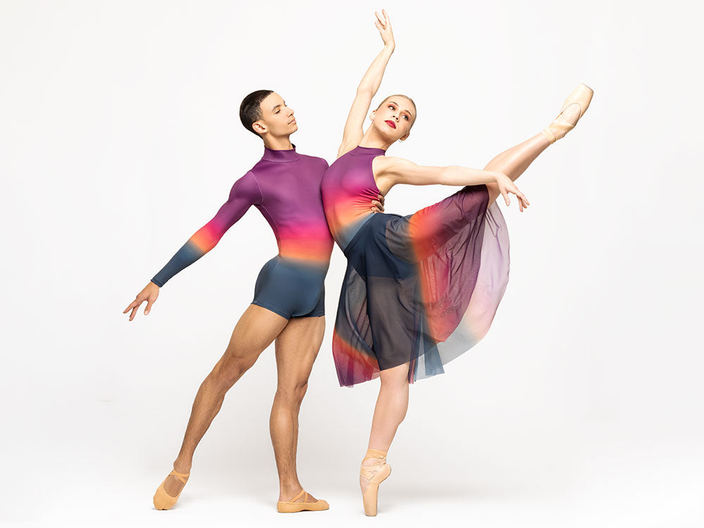 Female model is wearing rainbow ombre long full circle mesh skirt with matching ombre halter leotard. Male model is wearing matching ombre men's biketard with long sleeves, short inseam, and collar.