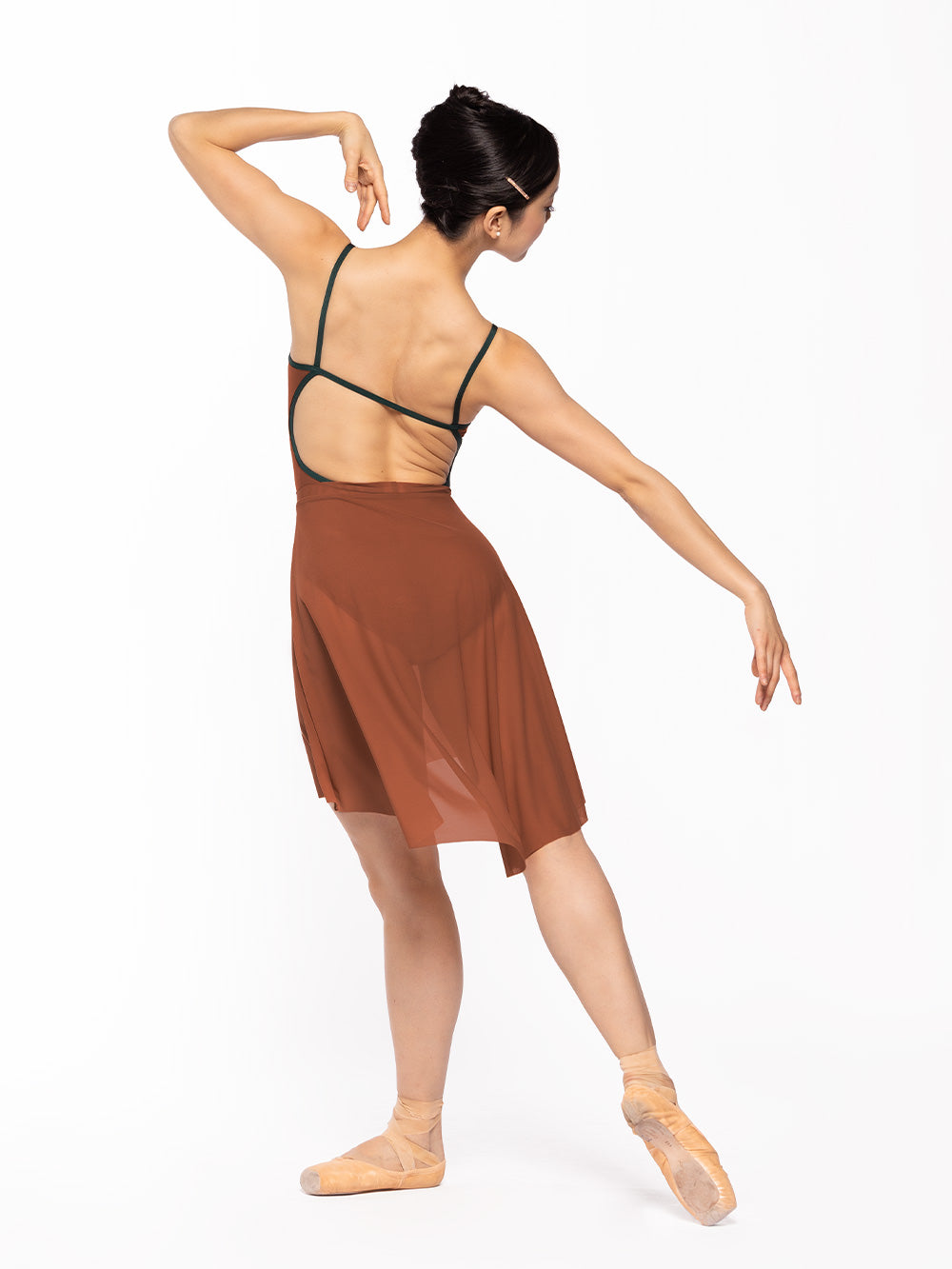 Dancer is facing diagonal back on tendu derriere with opposite arm on the shoulder, wearing a Candy Leotard Spice RTW.