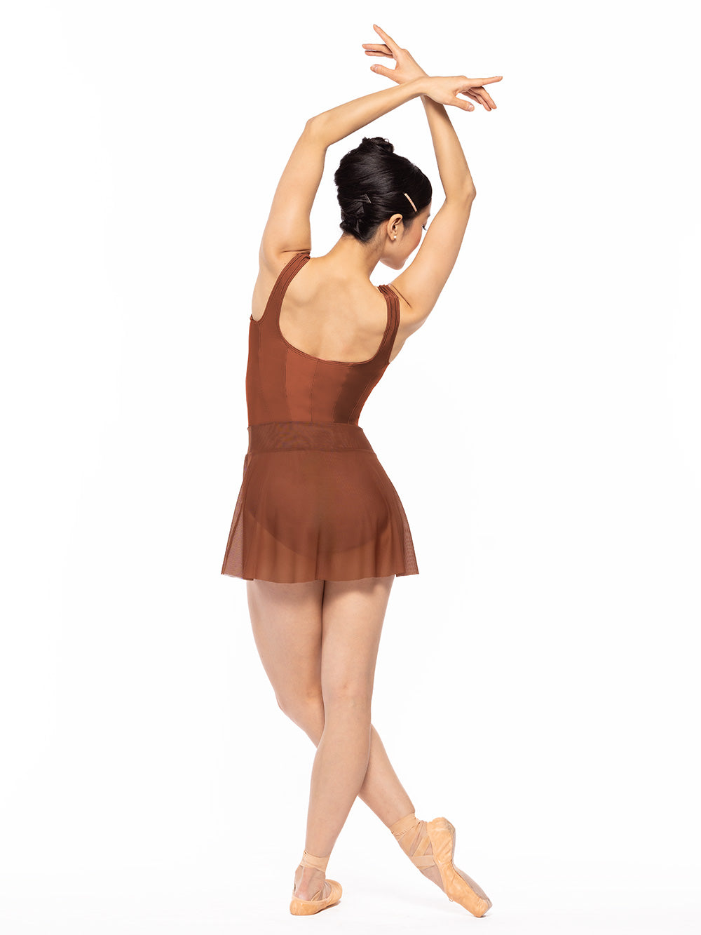 Dancer is facing back with one leg wrapped around the other on resting point, and arms on crossed fifth position, wearing a Diana Leotard Spice RTW.