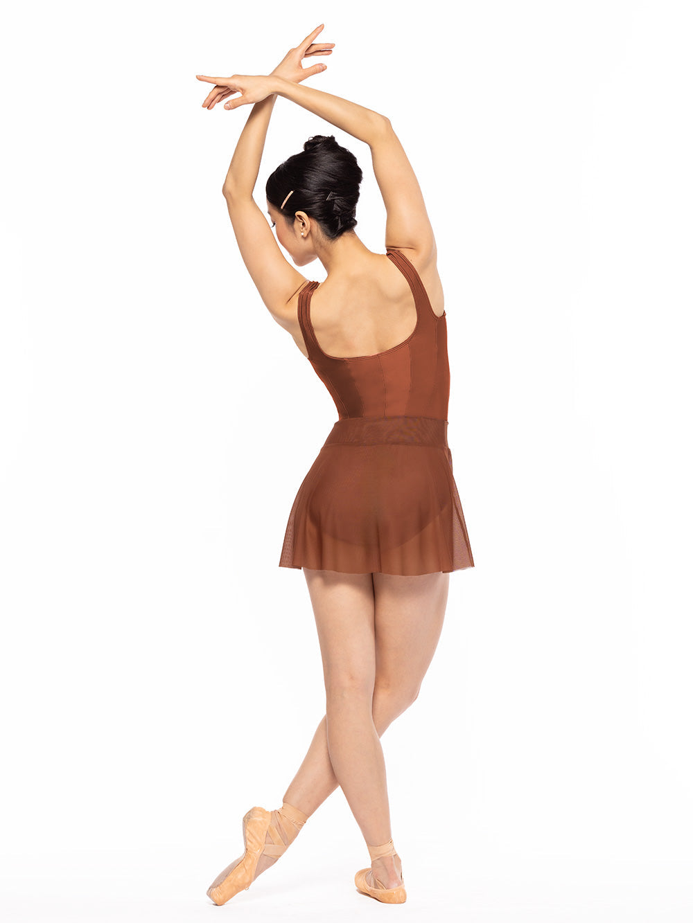Dancer is facing back with one leg crossed in front and both arms crossed in fifth position, wearing a Amora Skirt Spice Mesh RTW.