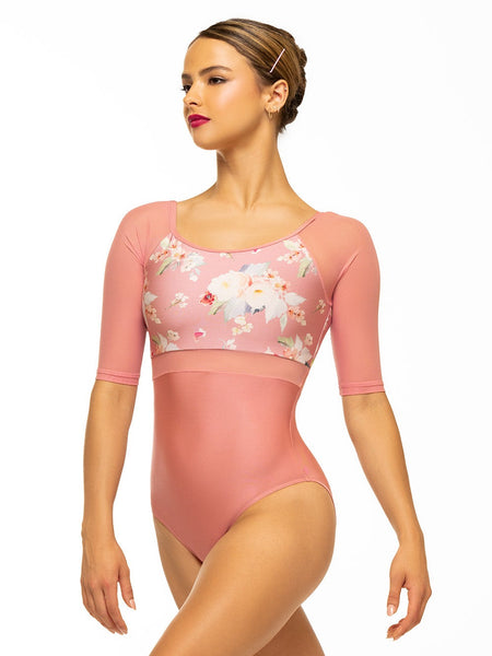 Model is wearing shiny pink bodysuit with floral print top, mesh middle and sleeves, and back keyhole detail.