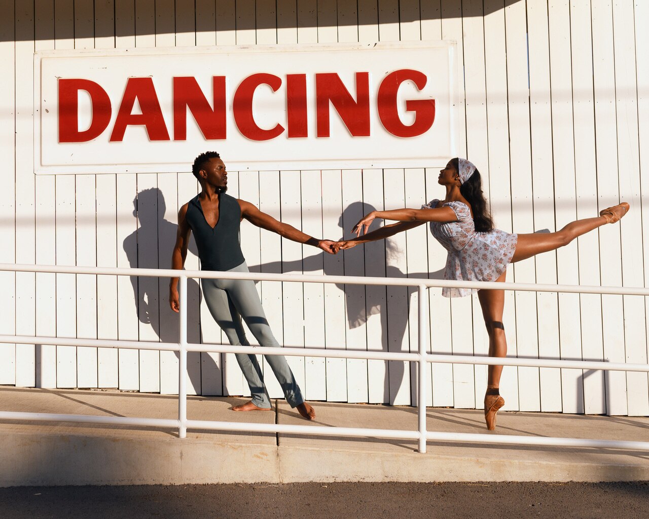Two models, one wearing a black top with a zipper and gray pants, the other model wearing a light blue floral pattern dress and matching headscarf