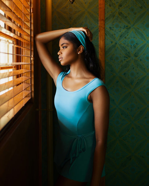 Model wearing a bright blue leotard with a matching wrap skirt and headband 