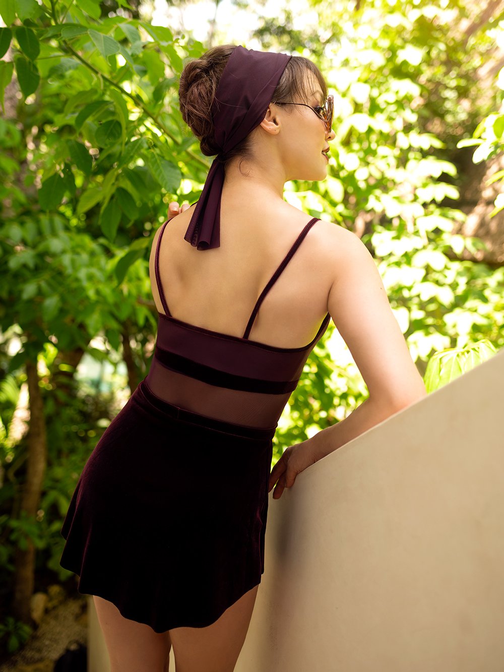 Model wearing a dark red leotard with velvet and mesh details with a matching dark red velvet skirt