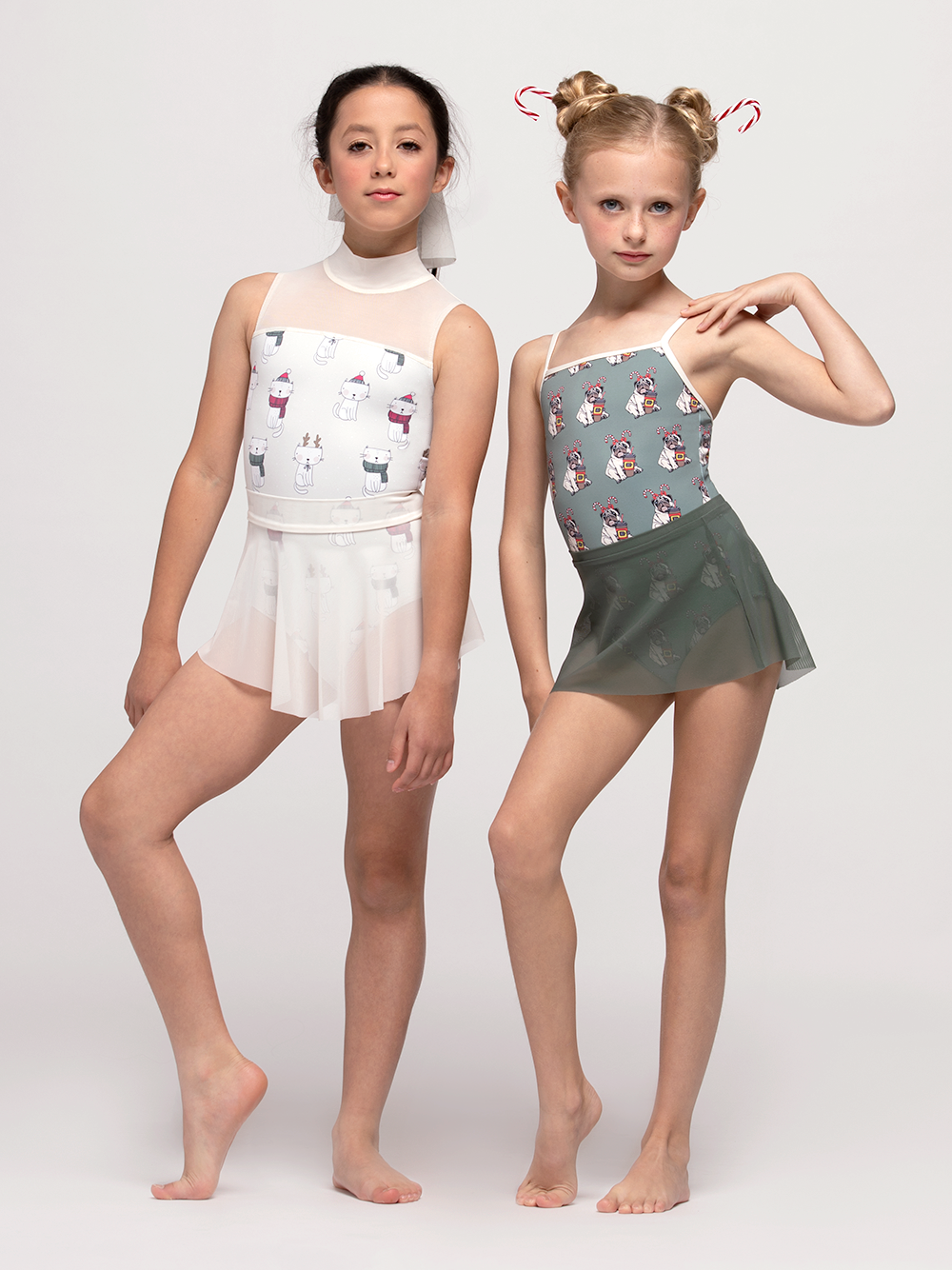 Two Models, one on left is in white holiday cat leotard with matching skirt, the one on the left is in holiday pug leotard and matching sage green skirt.