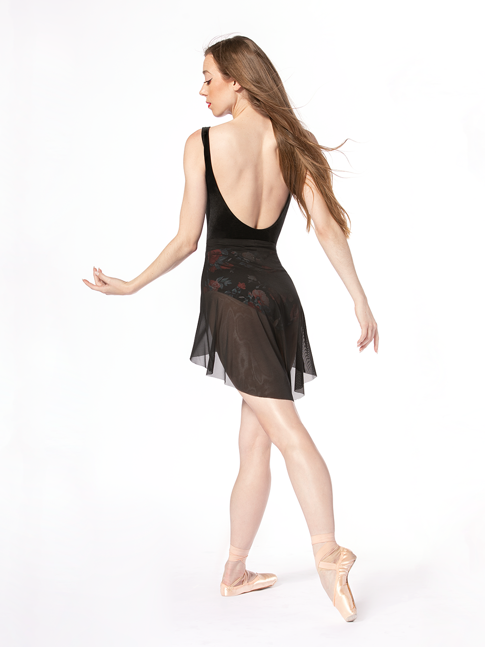 Dancer is facing back with tendu crossed derriere and arms to the side while head look to one of them, wearing a Mid High-Low Skirt Black Mesh RTW.