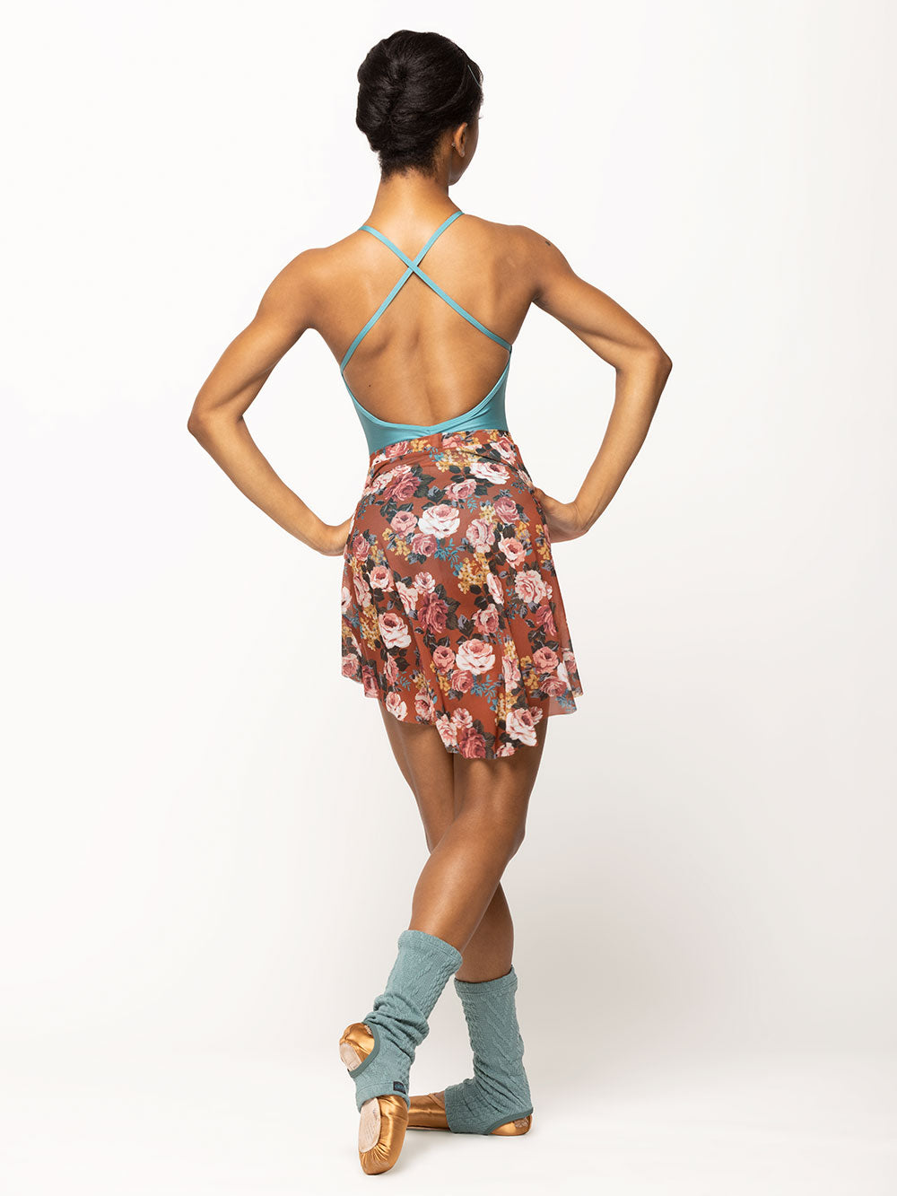 Back of model wearing shiny Caribbean blue leotard with open strappy back, copper floral pattern mesh skirt, and stirrup Ocean blue cable knit ankle warmers