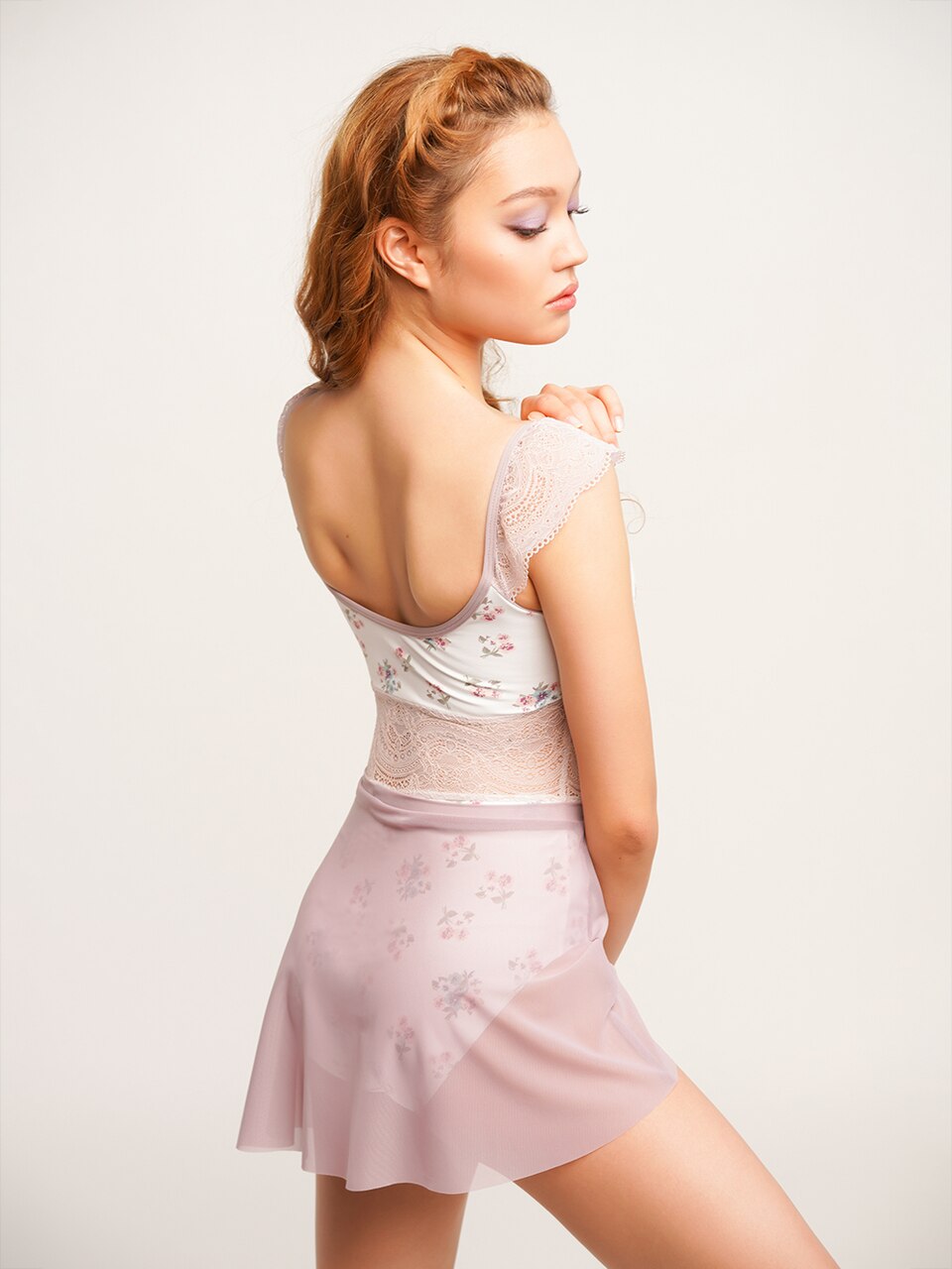 Model wearing white floral leotard with purple lace mid section and strap detail with purple mesh skirt