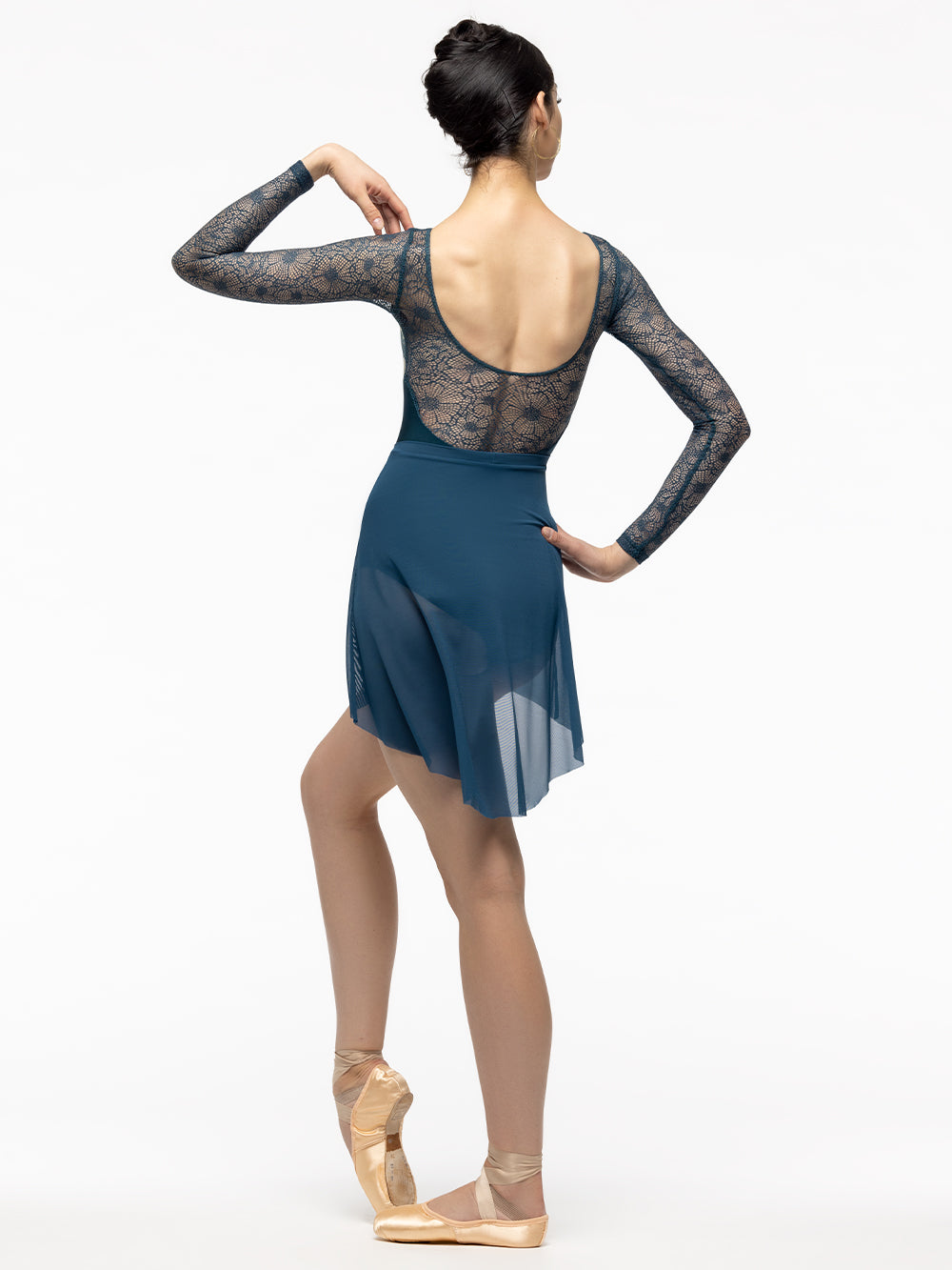 Back of model wearing shiny dark teal and gold floral print bodysuit with teal lace long sleeves, boat neck, and scoop back. Paired with matching dark blue green mesh high low skirt.