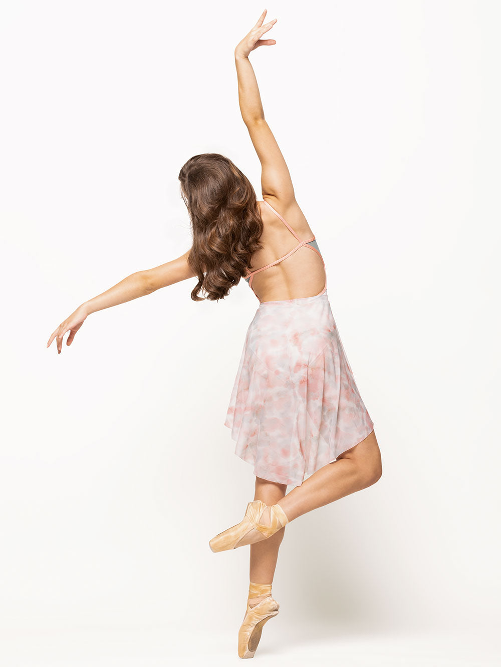 Back of model wearing a shiny rose watercolor print leotard with light pink cami straps, an open back, and light blue mesh back panels paired with a matching rose watercolor print mesh skirt