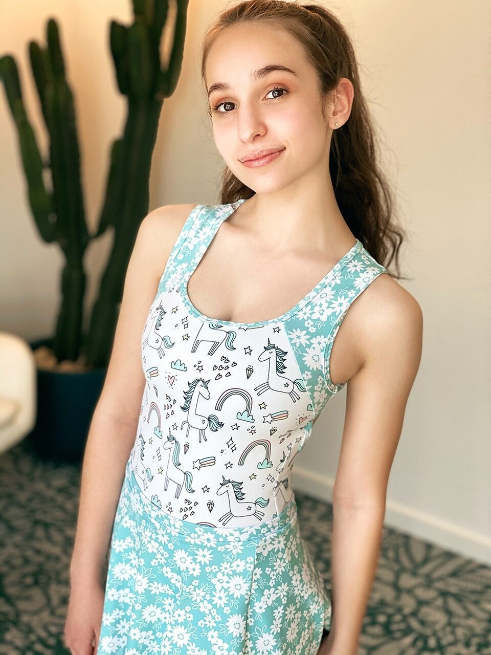 Model wearing a unicorn pattern leotard with blue floral straps and skirt