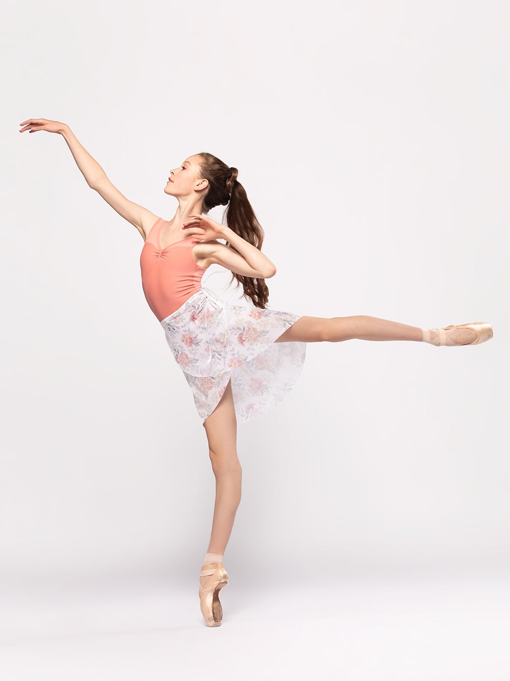Model wearing a light peach leotard with a matching floral print long mesh wrap skirt