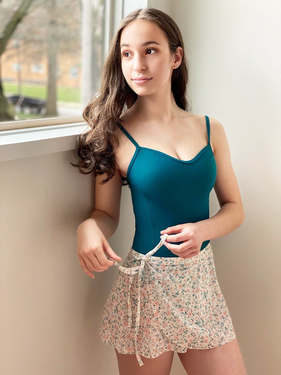 Model wearing a dark teal leotard with a floral wrap skirt