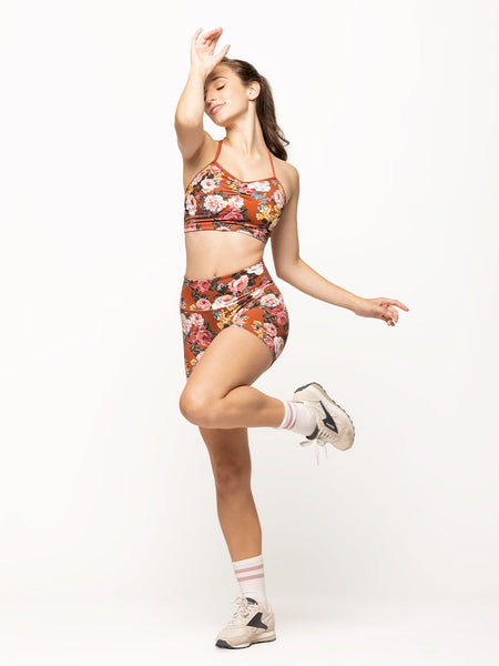Model is wearing bike shorts in picante orange floral print with wide waistband and a matching crop top with cami straps and pinch detail
