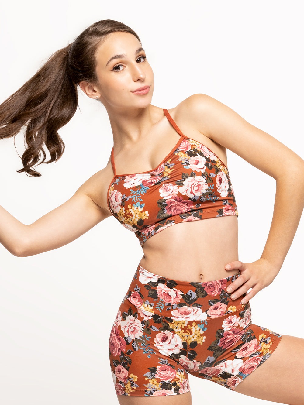 Model is wearing bike shorts in picante orange floral print with wide waistband and a matching crop top with cami straps and pinch detail