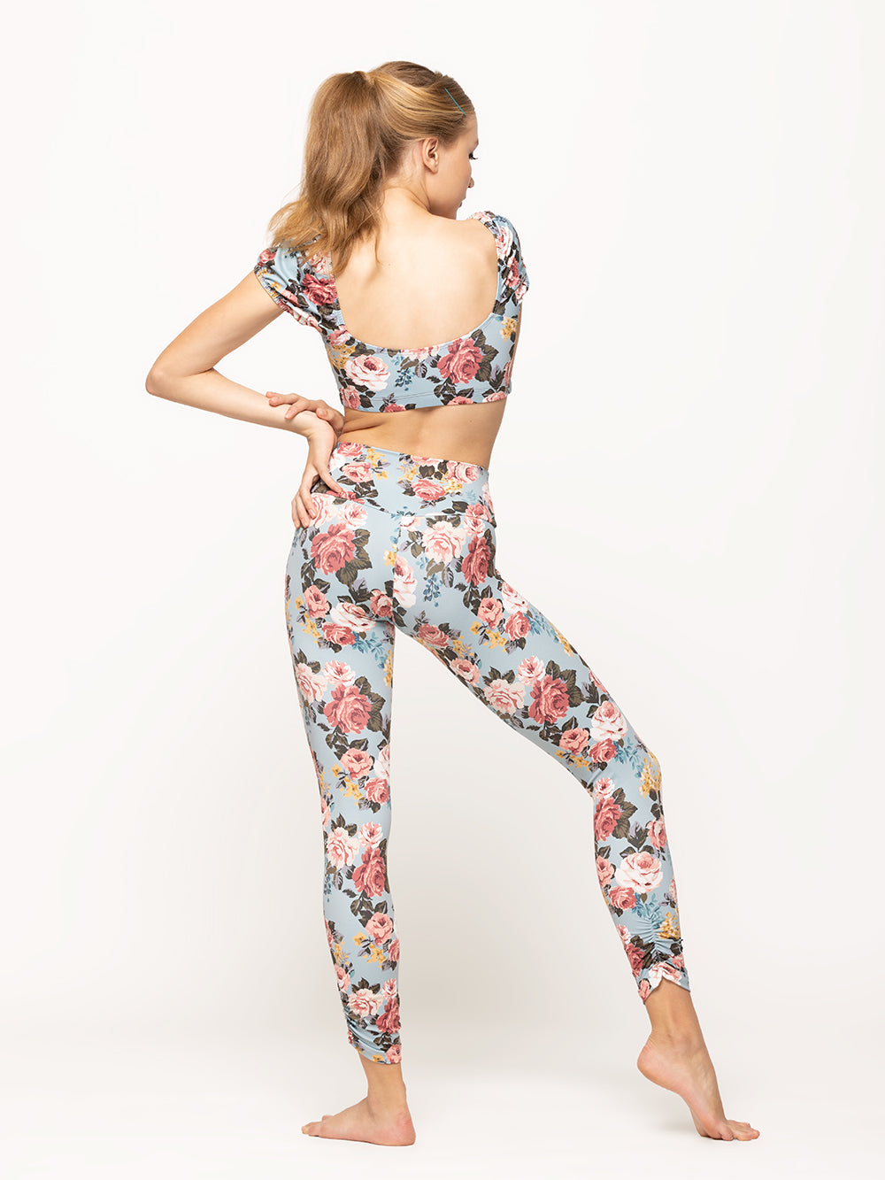 Back of model wearing light blue floral print short activewear crop top with puff sleeves and matching high waisted leggings