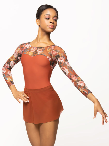 Model is wearing short deep orange tulip mesh dance skirt with matching orange and floral print long sleeve bodysuit