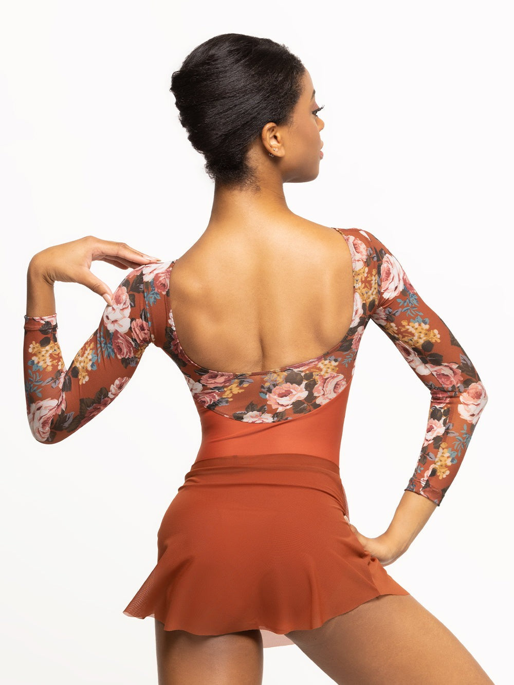 Back of model wearing short deep orange tulip mesh dance skirt with matching orange and floral print long sleeve bodysuit