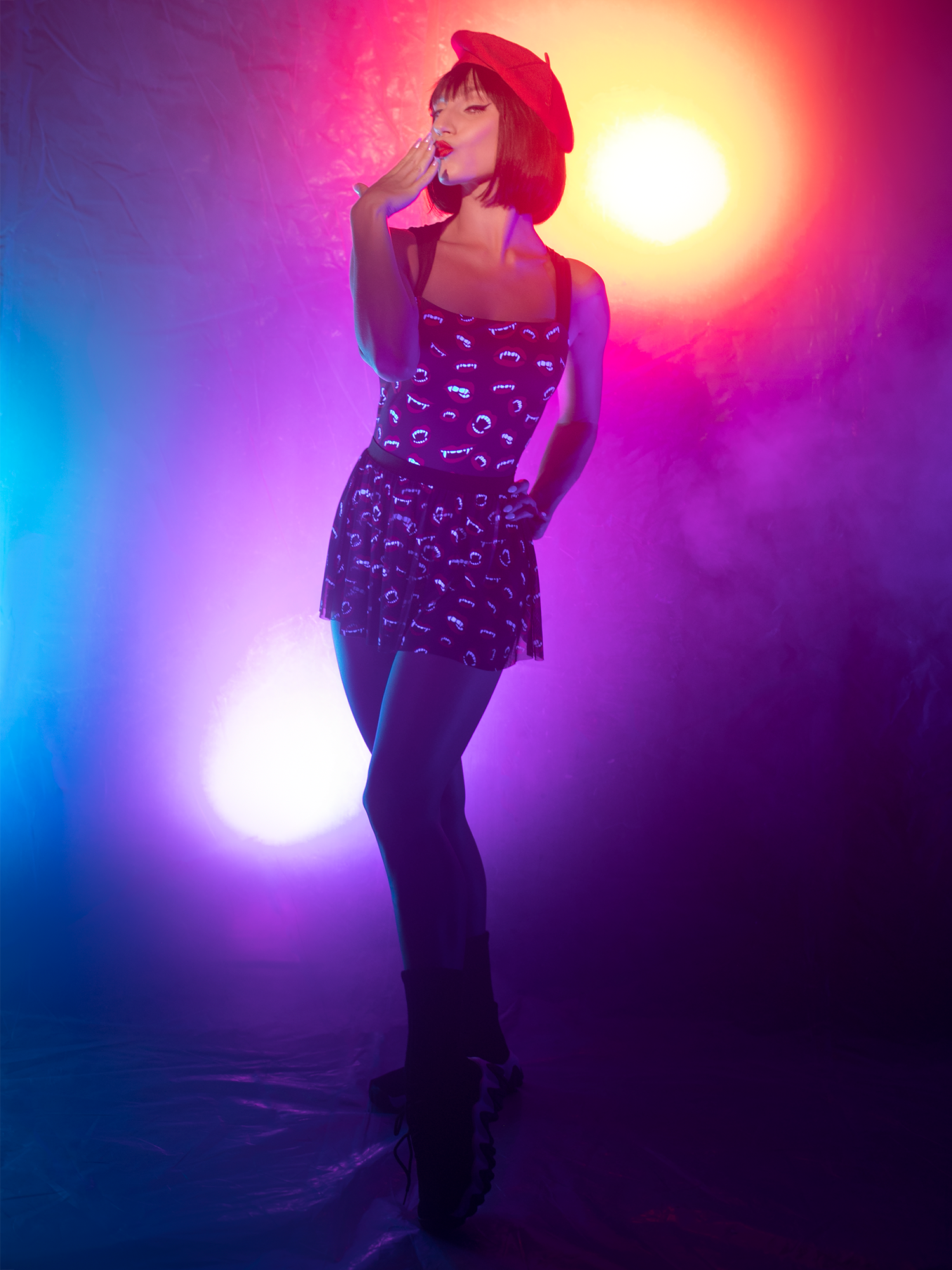 model in leotard and mesh skirt with with vampire  fangs and black background with hand on hip and to mouth
