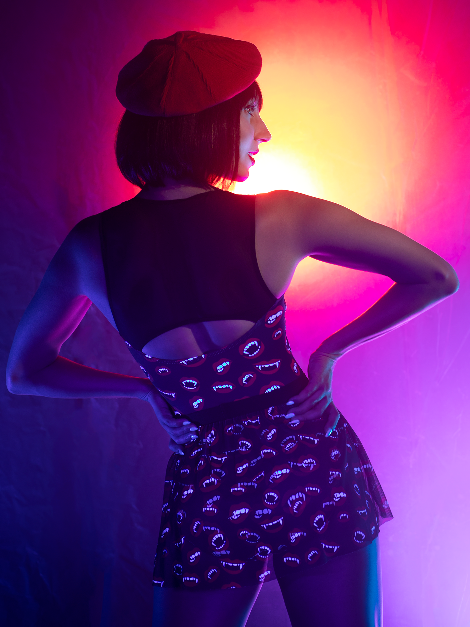 Back view of model in leotard and mesh skirt with with vampire  fangs and black background