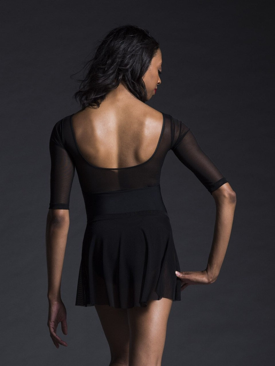 Dancer is facing back with one hand on the hip, wearing a Flare Skirt Black Mesh RTW.