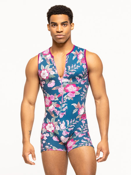 Model is wearing sleeveless short men's bodysuit in blue and magenta floral print with zipper front.