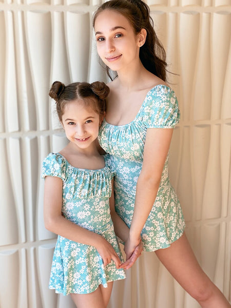 Two models, both wearing blue floral leotards with matching skirts