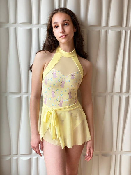 Model wearing a yellow Easter pattern leotard with mesh detail and a matching yellow mesh wrap skirt