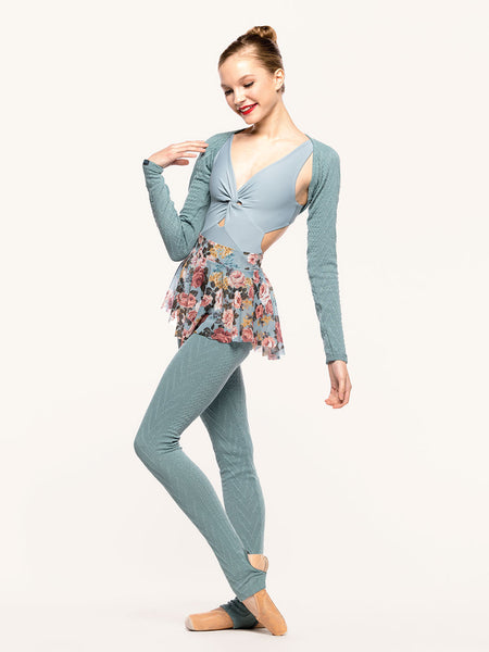 Model is wearing a cable knit shrug in Ocean blue green, light blue leotard with twist detail, light blue floral print mesh flare skirt, and matching Ocean knit long leg warmers