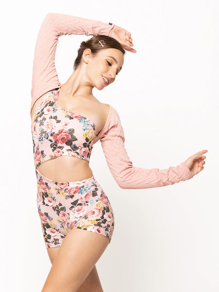 Model is wearing light pink cable knit shrug with light pink floral print cutout detail biketard